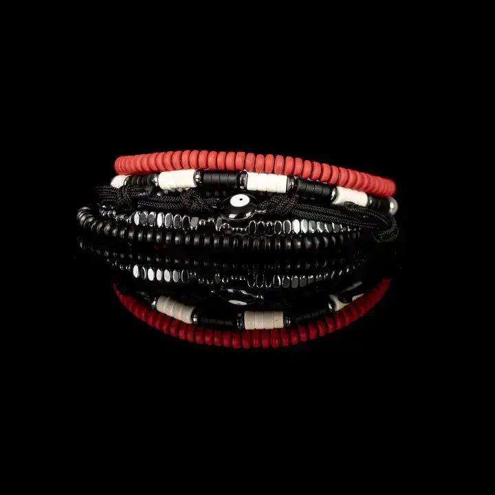 Men’s layered bracelet set featuring coral-red heishi beads, black braided cord wraps, black and white accent beads, faceted hematite crystal beads, black heishi beads, and an evil eye centerpiece, stacked in a bold contemporary bohemian luxury design on a white background.
