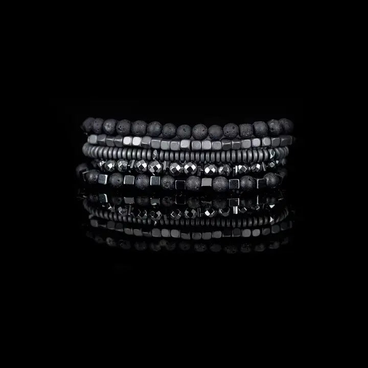 Black multi-layer men’s bracelet set featuring lava stone beads, faceted hematite stones, metallic cube accents, and layered gunmetal bead strands on a light background.