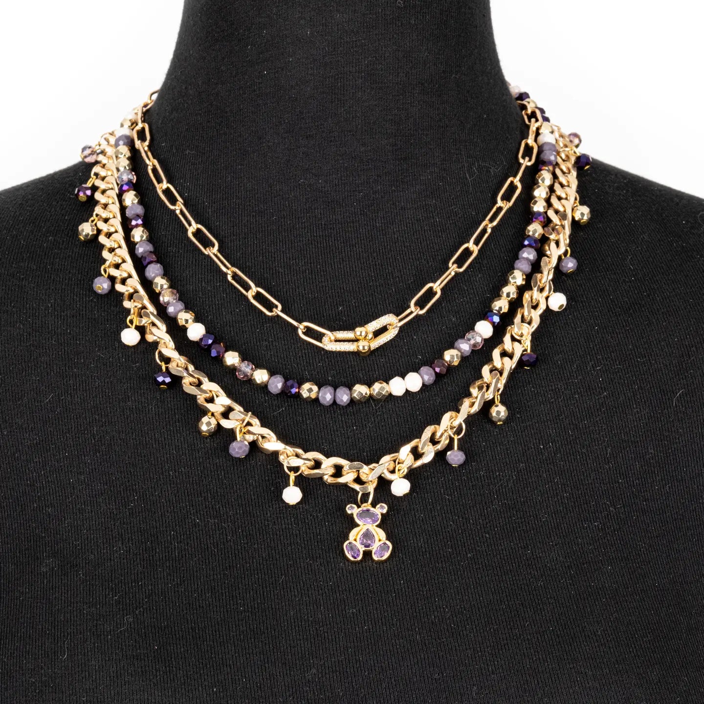 Layered gold necklace with purple crystal beads and small bear charm on white background.
