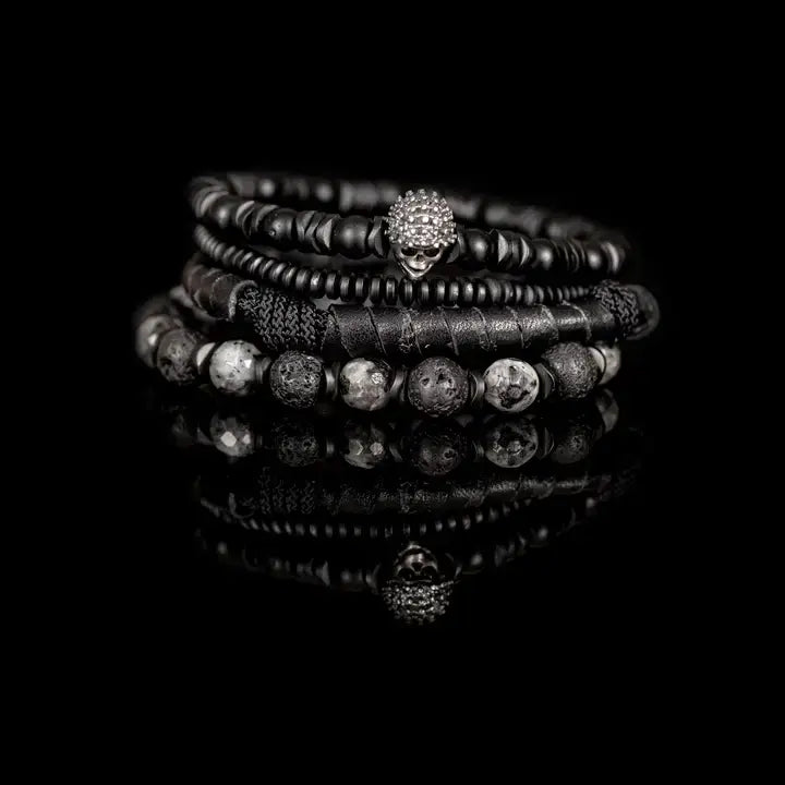 Black multi-layer men’s bracelet featuring crystal skull centerpiece, lava stone beads, marble grey natural stones, wrapped leather layer, and matte black bead strands on a light background.