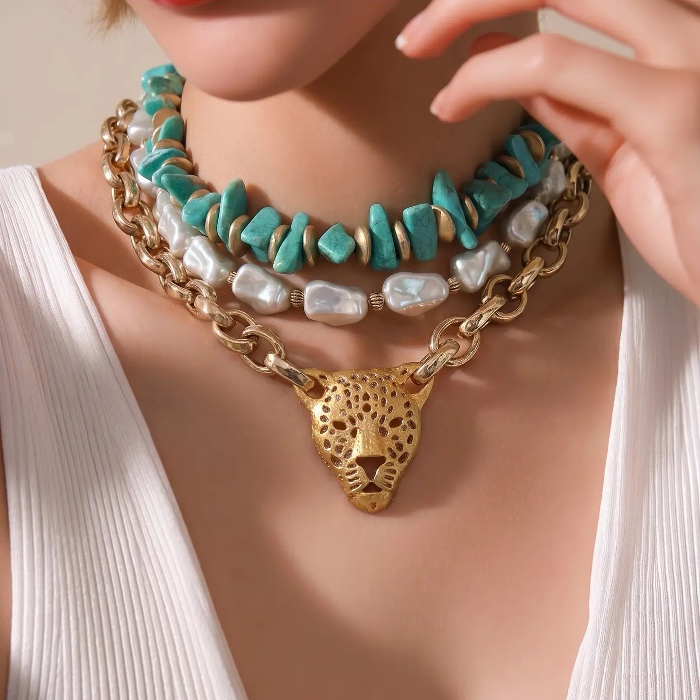 Layered turquoise and pearl necklace with gold chain and leopard head pendant on a white background.