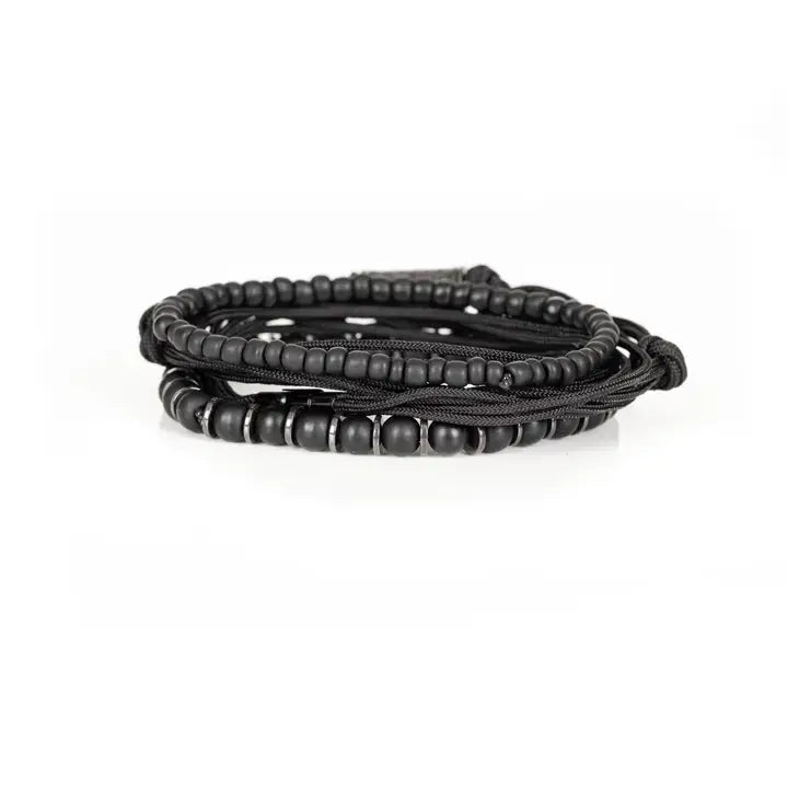 Black layered men’s bracelet set with matte black beads, braided rope wraps, metallic spacer accents, and pavé cylindrical centerpiece on white background.