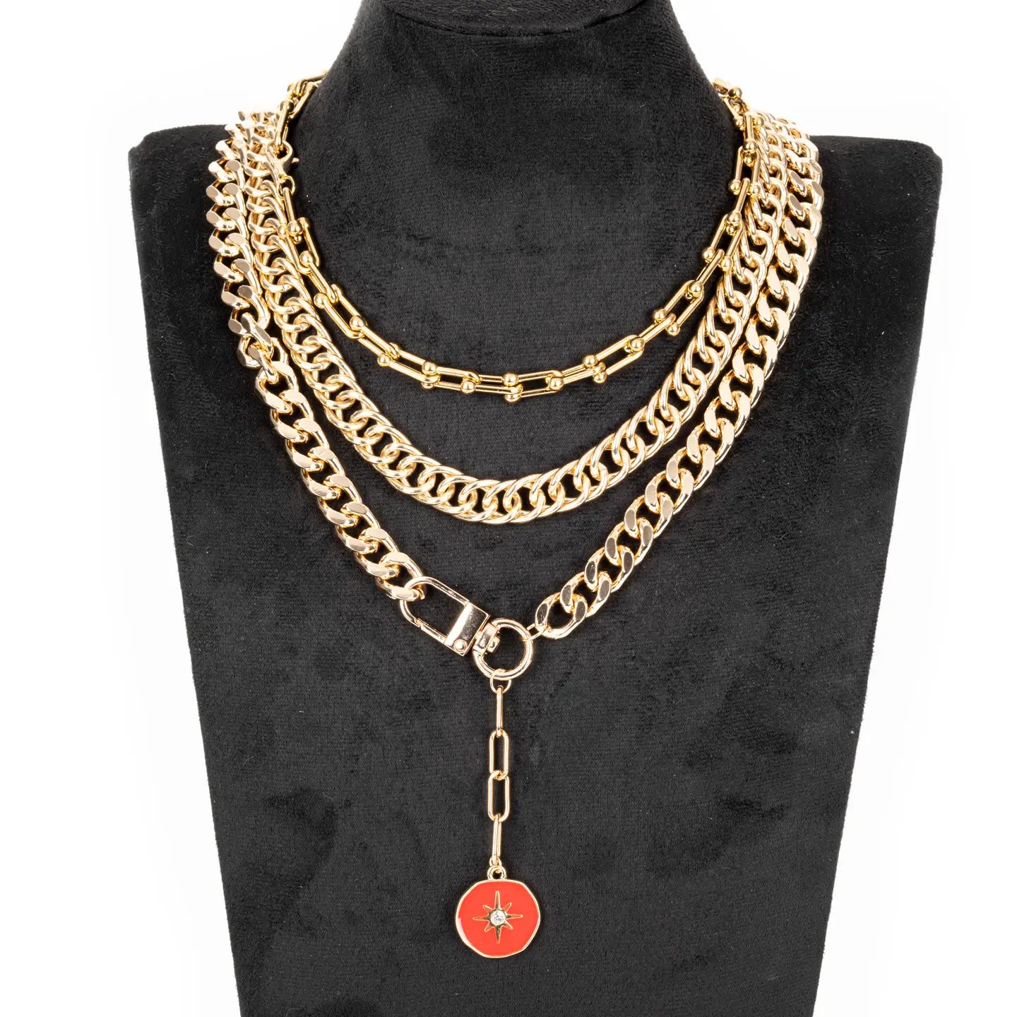 Layered gold chain necklace with multiple chain styles and a red enamel charm drop, displayed on a white background.