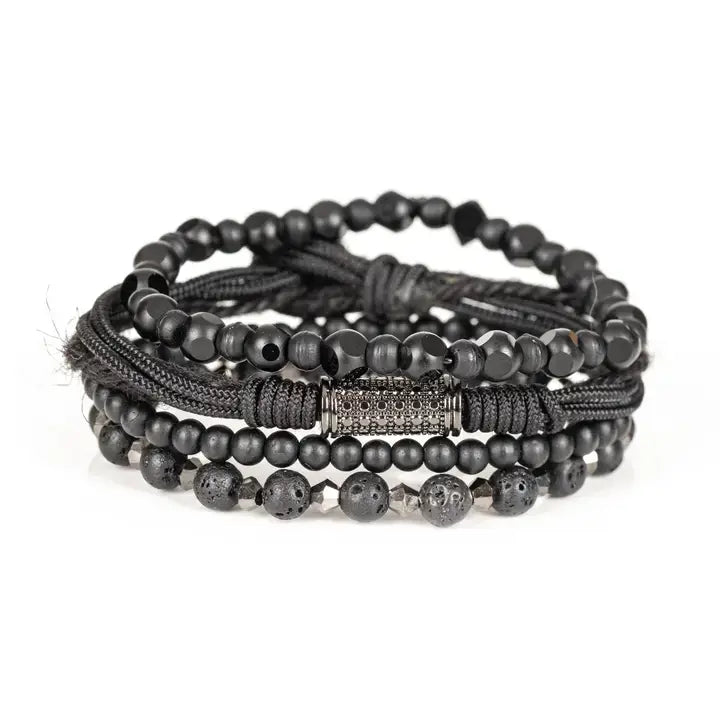 Black layered men’s bracelet set with matte black beads, lava stone accents, faceted geometric beads, braided rope wraps, and pavé cylindrical centerpiece on white background.