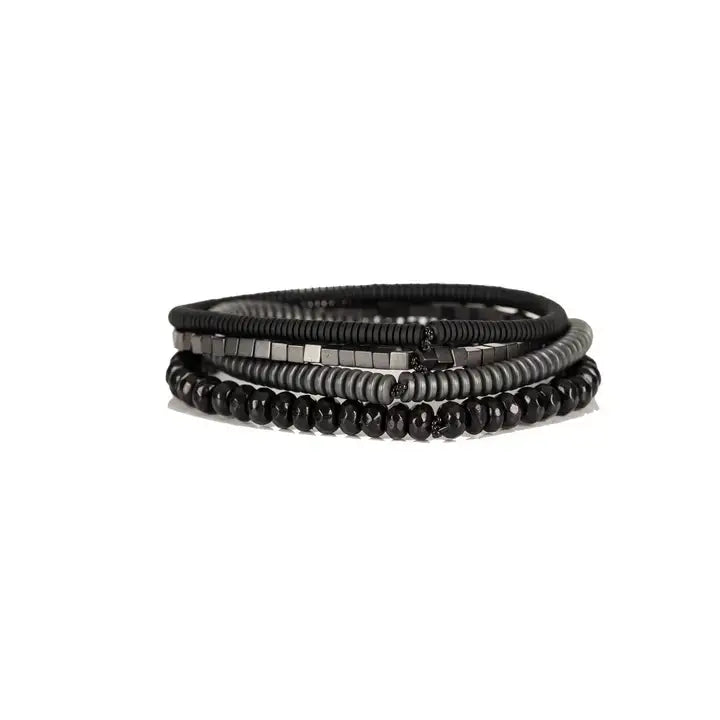 Men's black and gunmetal layered bracelet set featuring black leather, matte black heishi beads, gunmetal cube beads, metallic disc beads, and faceted black crystal beads in a sleek stacked design on a white background.
