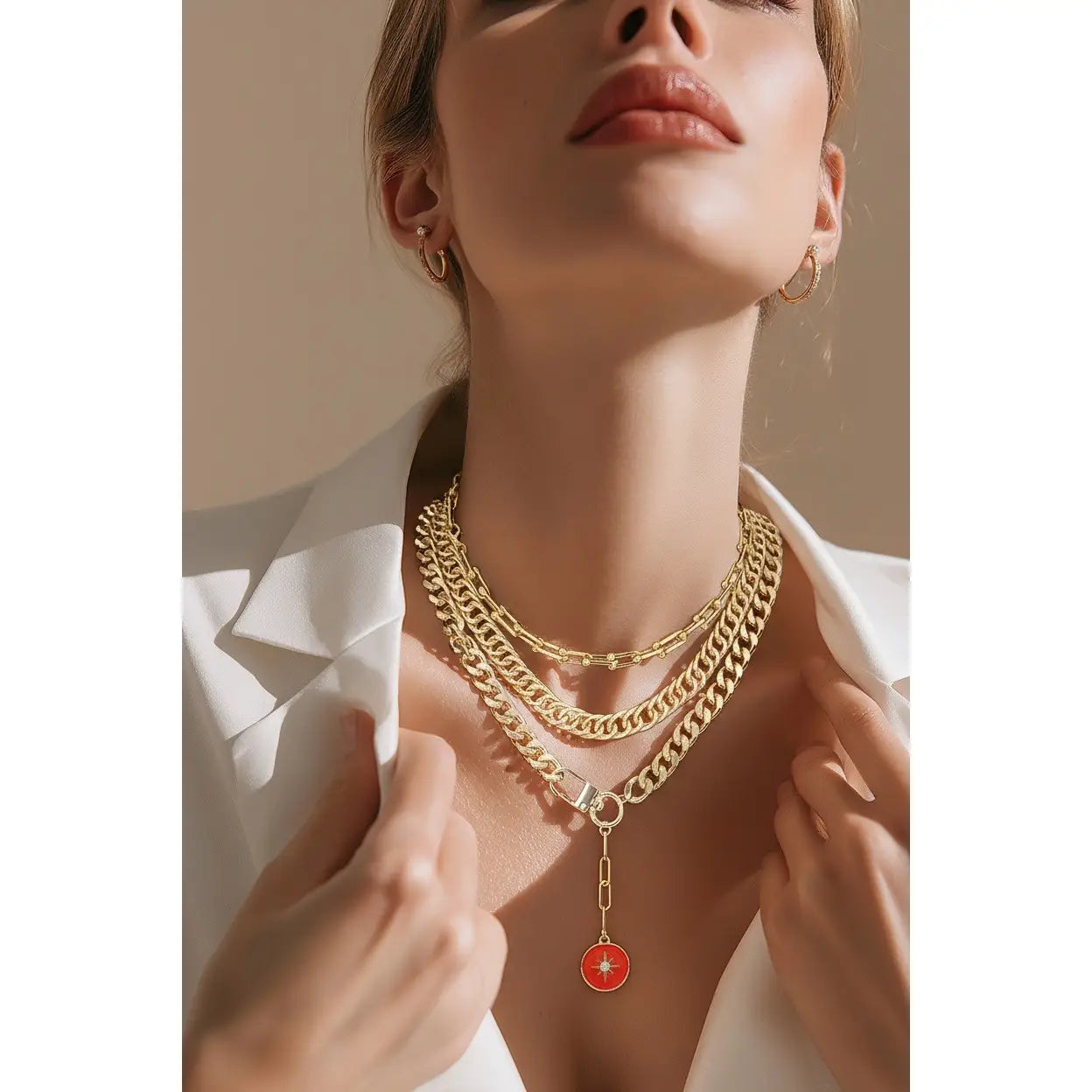 Layered gold chain necklace with multiple chain styles and a red enamel charm drop, displayed on a white background.