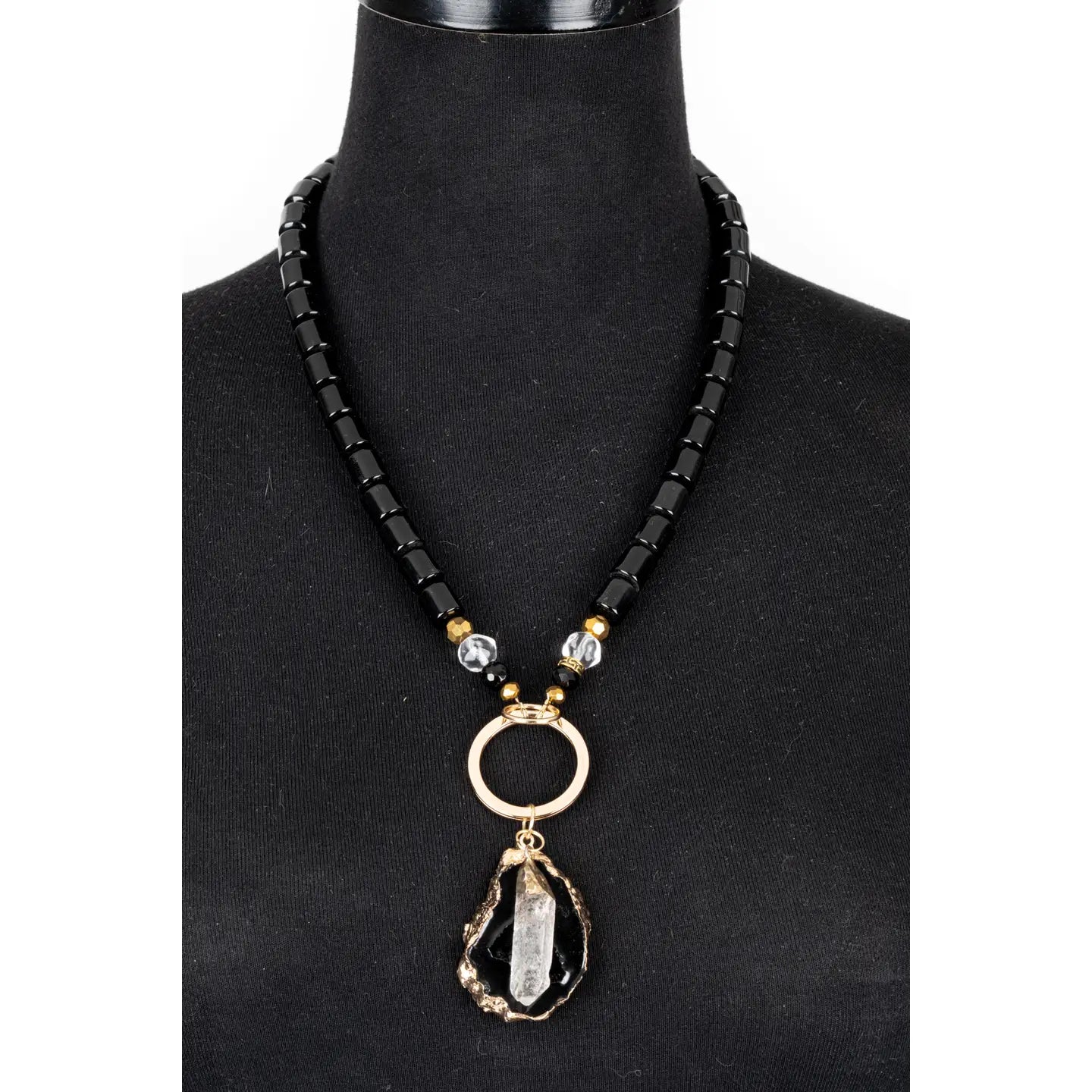 Black beaded necklace with gold ring connector and raw stone crystal pendant on white background.