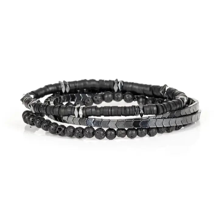 Black multi-layer men’s bracelet featuring hematite disc strands, shield-pattern metallic beads, pyramid-cut spacers, and lava stone bead accents on a light background.