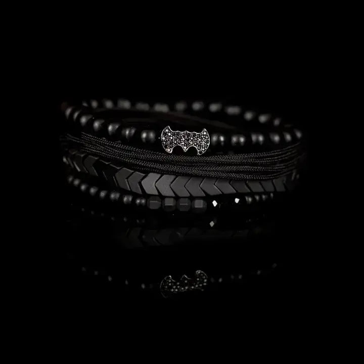 Black layered men’s bracelet set with matte black beads, Batman-inspired centerpiece, chevron metallic beads, crystal accents, and braided rope wraps on white background.