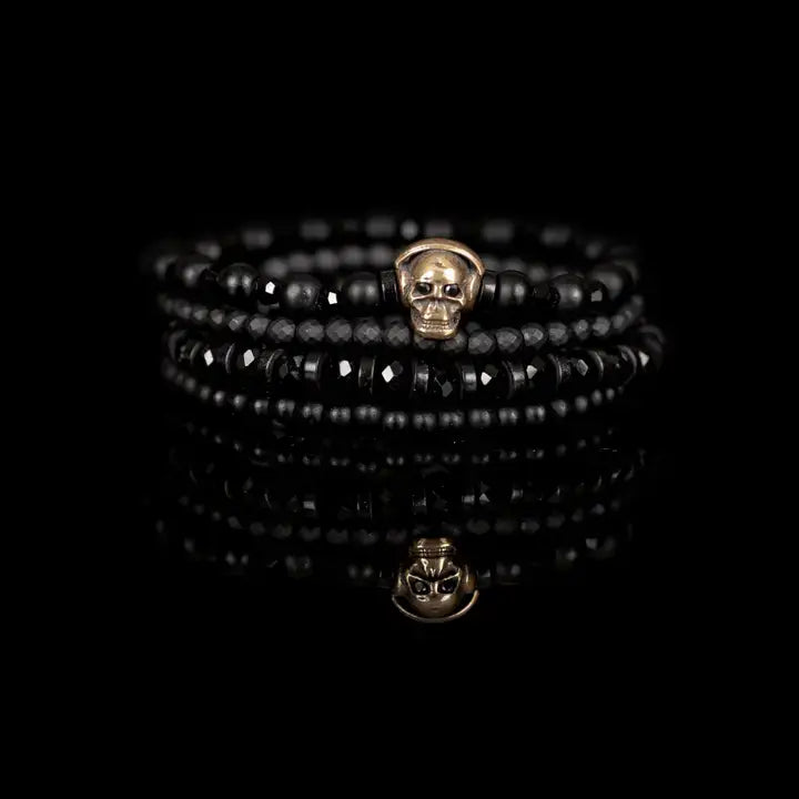 Black layered men’s bracelet set with matte black beads, gold skull centerpiece, faceted crystal accents, and geometric spacer beads on white background.