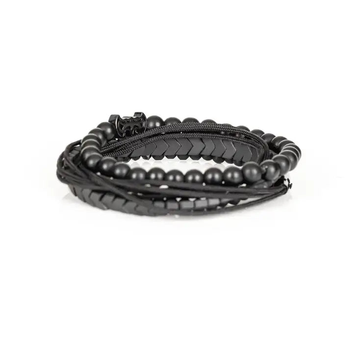 Black layered men’s bracelet set with matte black beads, Batman-inspired centerpiece, chevron metallic beads, crystal accents, and braided rope wraps on white background.
