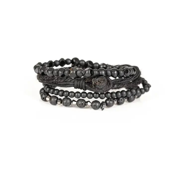 Black layered men’s bracelet set with matte black beads, lava stone accents, faceted geometric beads, braided rope wraps, and pavé cylindrical centerpiece on white background.