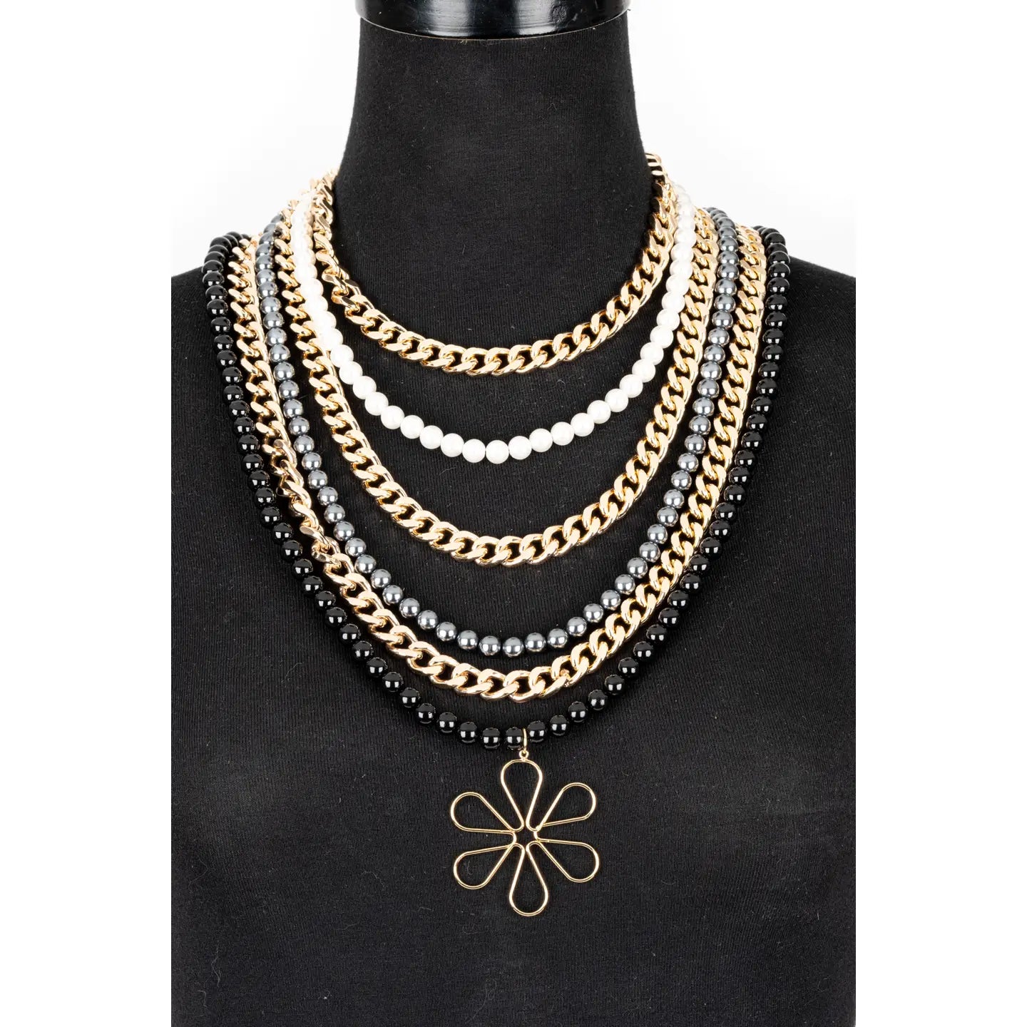 Multi-layer necklace with black, white, and metallic beads and chains, featuring a floral pendant, displayed on a white background.