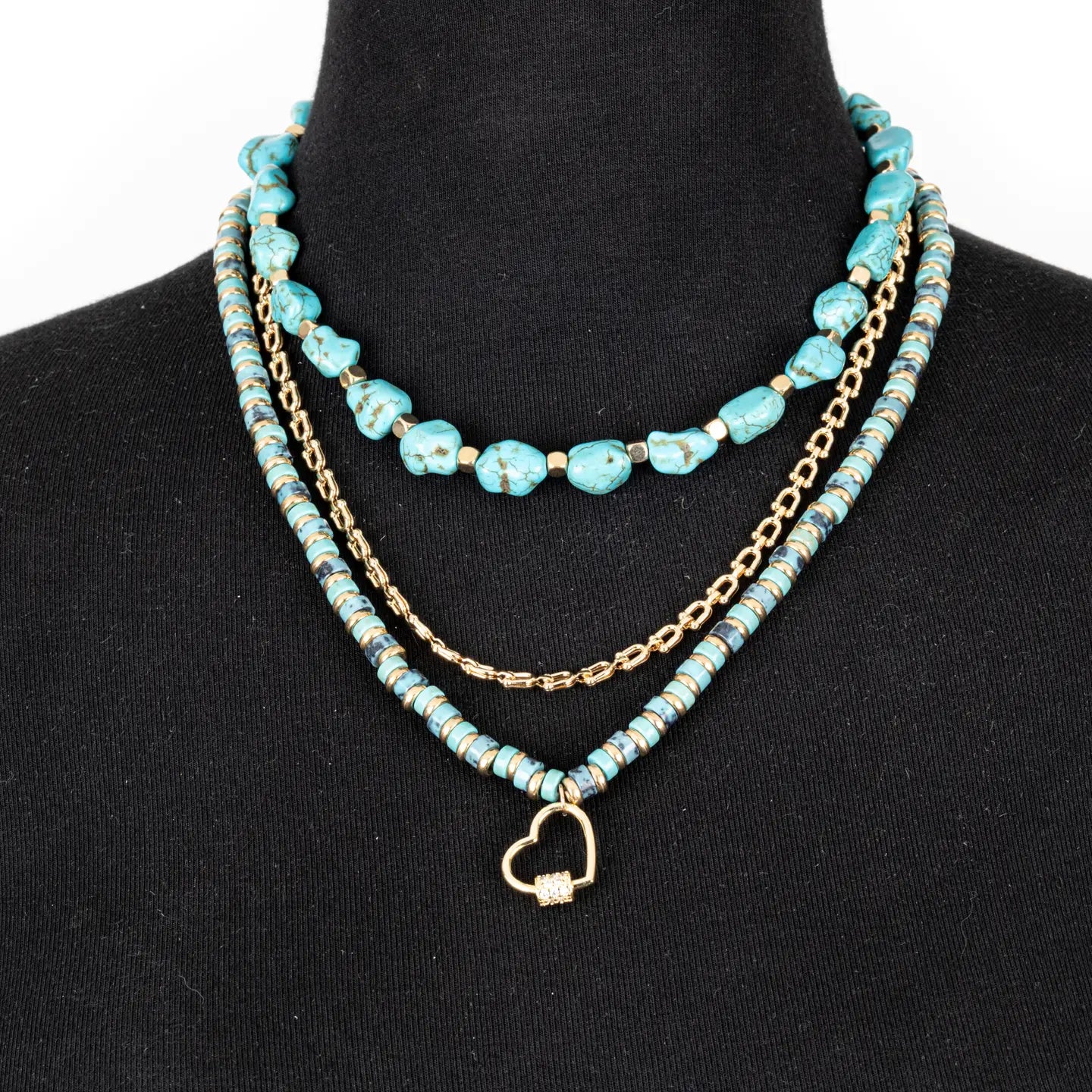 Layered turquoise bead necklace with gold chain and small heart charm on white background.