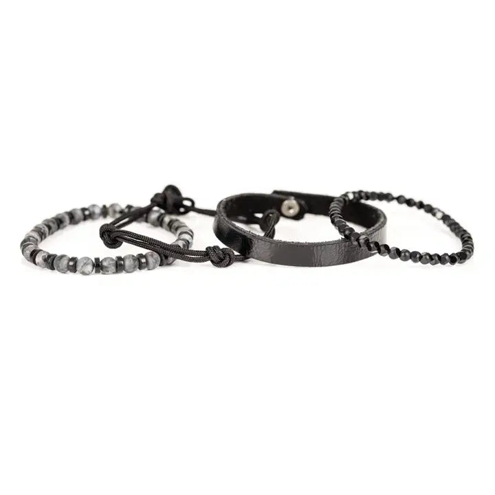 Black multi-layer men’s bracelet featuring faceted black onyx beads, textured black leather band, braided rope layers, marble grey natural stone beads, and metallic spacer accents on a light background.