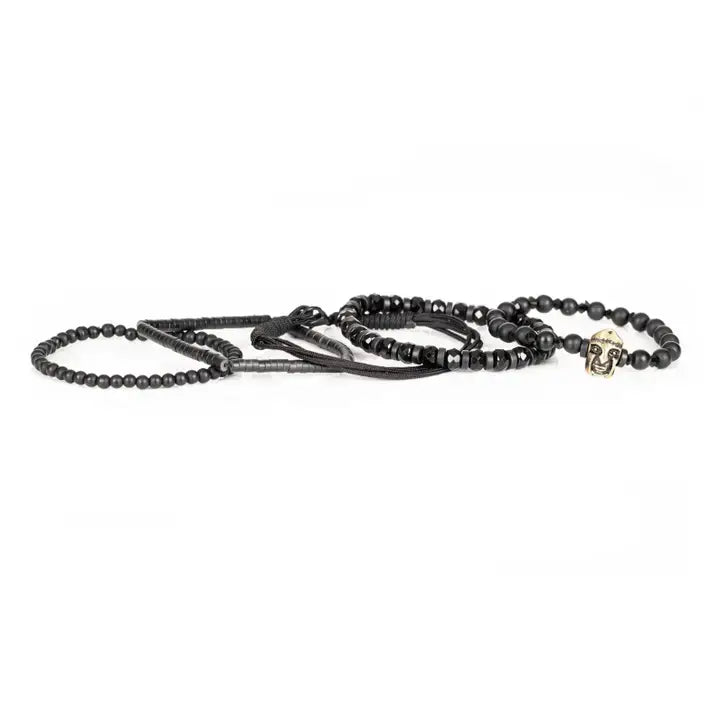 Black multi-layer men’s bracelet featuring matte black beads, faceted onyx stones, metallic tribal mask centerpiece, braided rope layers, and hematite bead strands on a light background.