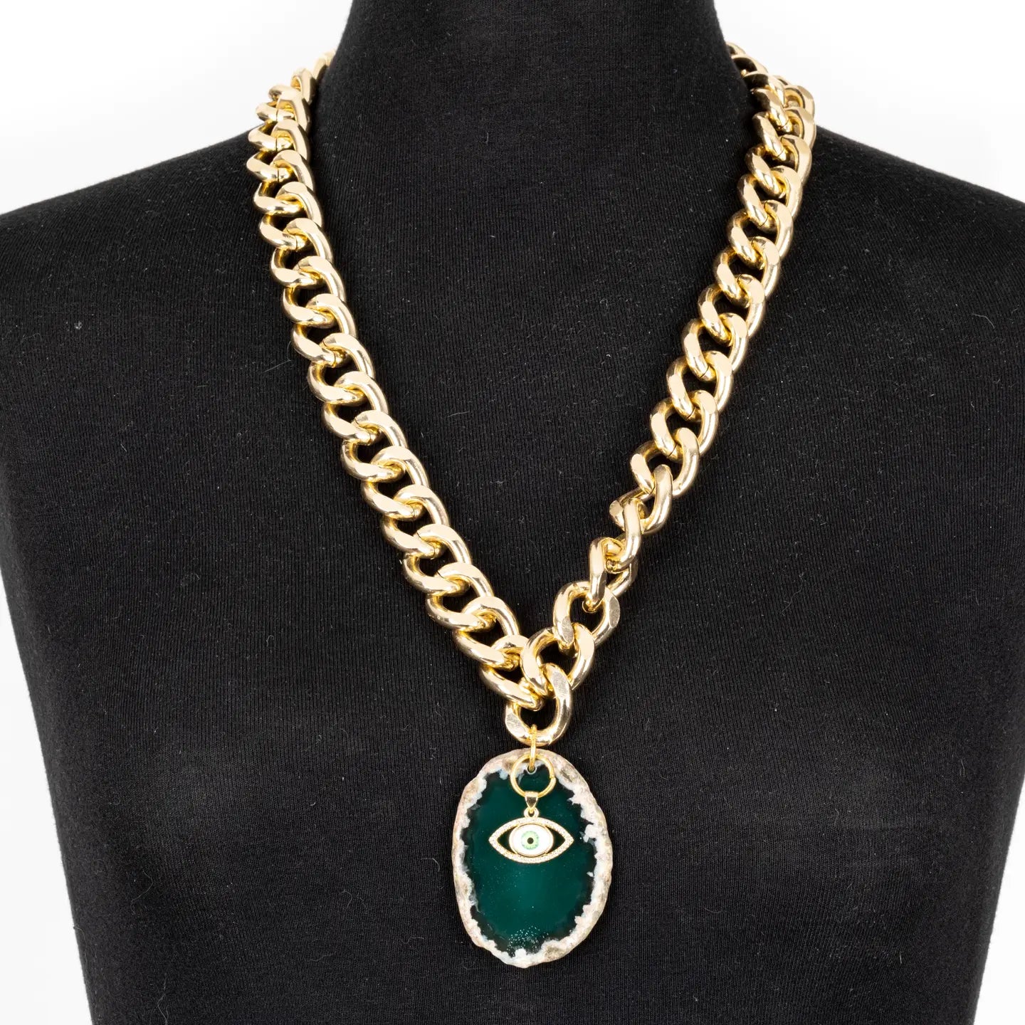 Gold chunky chain necklace with green stone pendant and evil eye charm on white background.