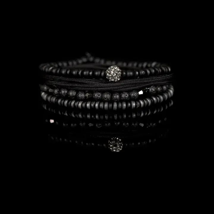 Black multi-layer men’s bracelet featuring matte black beads, lava stone accents, crystal centerpiece bead, braided rope layers, faceted metallic details, and hematite disc strands on a light background.