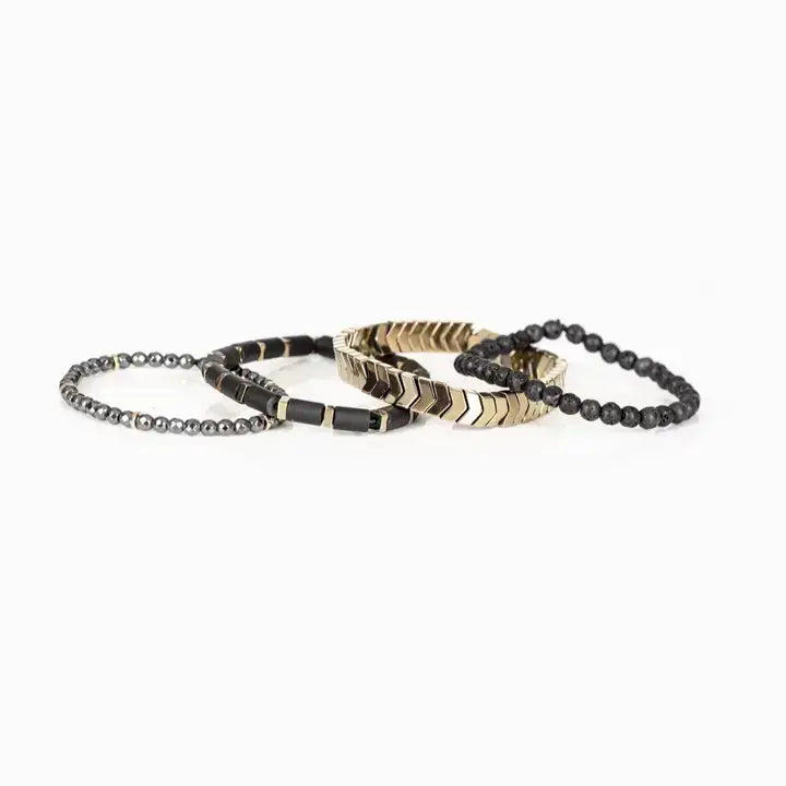 Men’s layered bracelet set featuring matte black lava stone beads, gold-tone chevron metal beads, black cylindrical beads with gold spacers, and faceted hematite beads, stacked in a modern luxury design on a white background.
