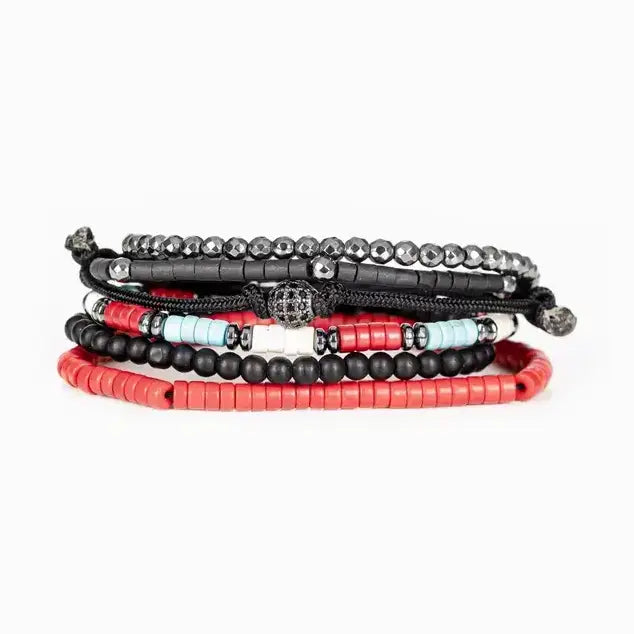 Men’s layered bracelet set featuring faceted hematite crystal beads, black heishi beads, turquoise and coral-red accent beads, matte black bead strands, black braided cord wraps, and a pavé-style gunmetal centerpiece, stacked in a bold contemporary bohemian luxury design on a white background.