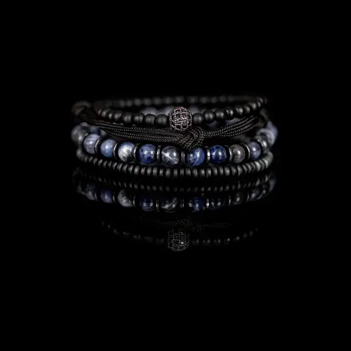 Black and blue layered men’s bracelet set with matte black beads, blue marbled stone accents, braided rope wraps, and pavé centerpiece on white background.