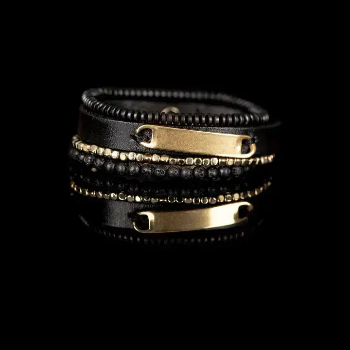 Men’s layered bracelet set featuring a black leather cuff with a polished gold-tone ID plate, matte black lava stone beads, gold-tone hematite spacer beads, and black heishi beads, stacked in a sophisticated black and gold luxury design on a white background.