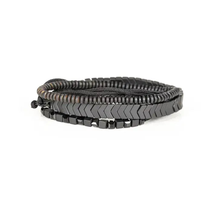 Men’s layered bracelet set featuring gunmetal chevron metal beads, black hematite cube beads, dark metallic heishi beads, black braided cord, and a pavé-style gunmetal accent bead, stacked in a sleek monochromatic luxury design on a white background.