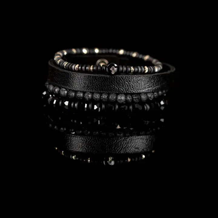 Men’s layered bracelet set featuring a black textured leather cuff, matte black lava stone beads, faceted black crystal beads, hematite accents, and a black beaded strand with a cross charm, stacked in a bold modern luxury design on a white background.