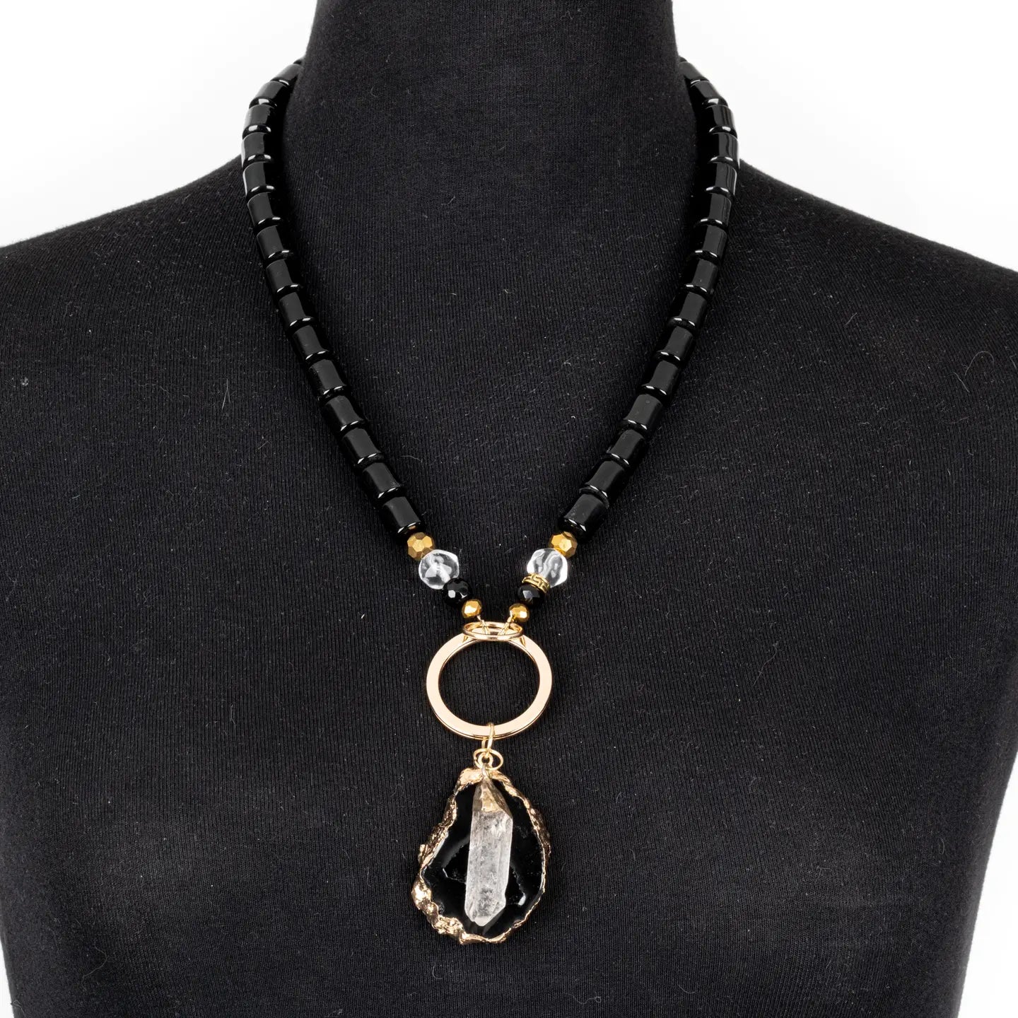 Black beaded necklace with gold ring connector and raw stone crystal pendant on white background.
