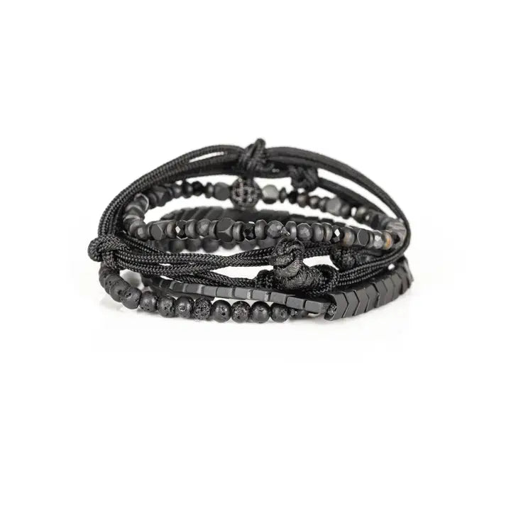 Black layered men’s bracelet set with chevron metal strand, lava stone beads, faceted metallic accents, braided rope wraps, and pavé centerpiece on white background.