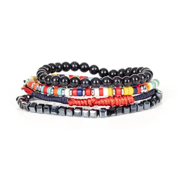 Men’s layered bracelet set featuring glossy black onyx-style beads, multicolor seed beads, red woven cord, navy braided cord, and faceted hematite cube beads, stacked in a bold contemporary luxury design on a white background.