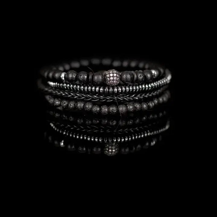 Black layered men’s bracelet set with lava stone beads, braided leather, hematite accents, matte black beads, and pavé centerpiece on white background.