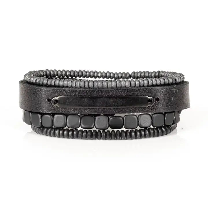 Black multi-layer men’s bracelet featuring textured leather band, gunmetal plate detail, layered hematite bead strands, and cube-cut black beads on a light background.