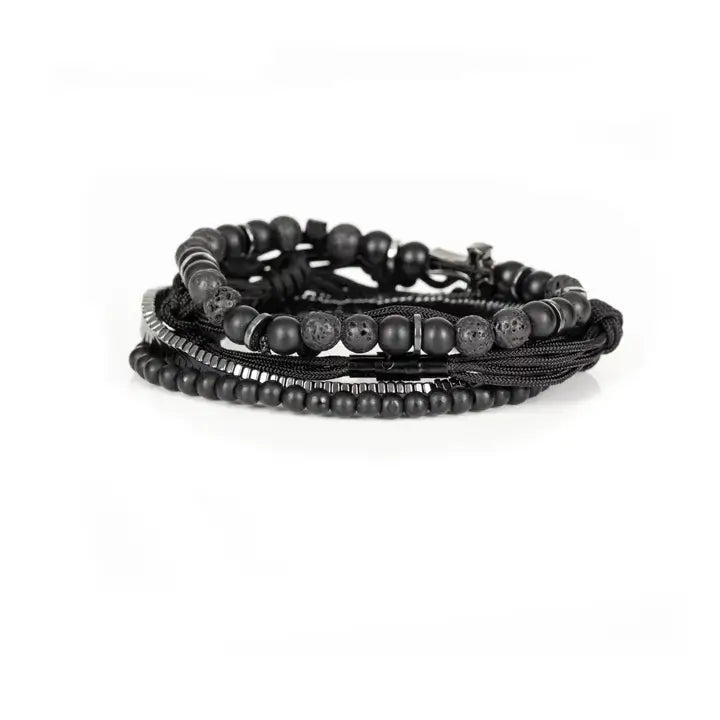 Black layered men’s bracelet set with pavé cross detail, silver chevron metal strand, lava stone beads, matte black beads, and braided rope wraps on white background.