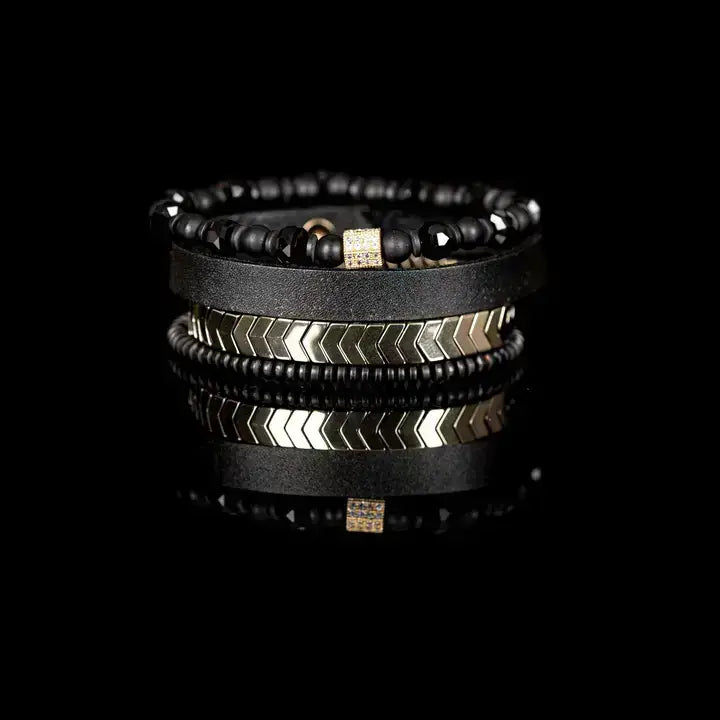 Black multi-layer men’s bracelet featuring faceted black onyx beads, black leather band, gold chevron metal bar, crystal cube accent, and layered metallic bead details on a light background.