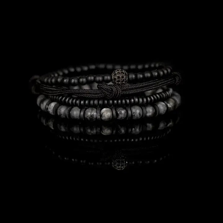 Black and gray layered men’s bracelet set with matte black beads, gray marbled stone accents, braided rope wraps, metallic spacers, and pavé centerpiece on white background.