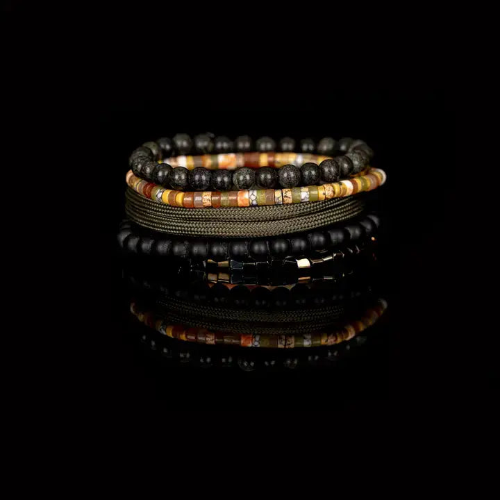 Men’s layered bracelet set featuring black natural stone beads, matte black onyx-style beads, multicolor heishi beads in warm earth tones, olive braided cord wraps, and metallic hematite spacer beads, stacked in a contemporary bohemian luxury design on a white background.