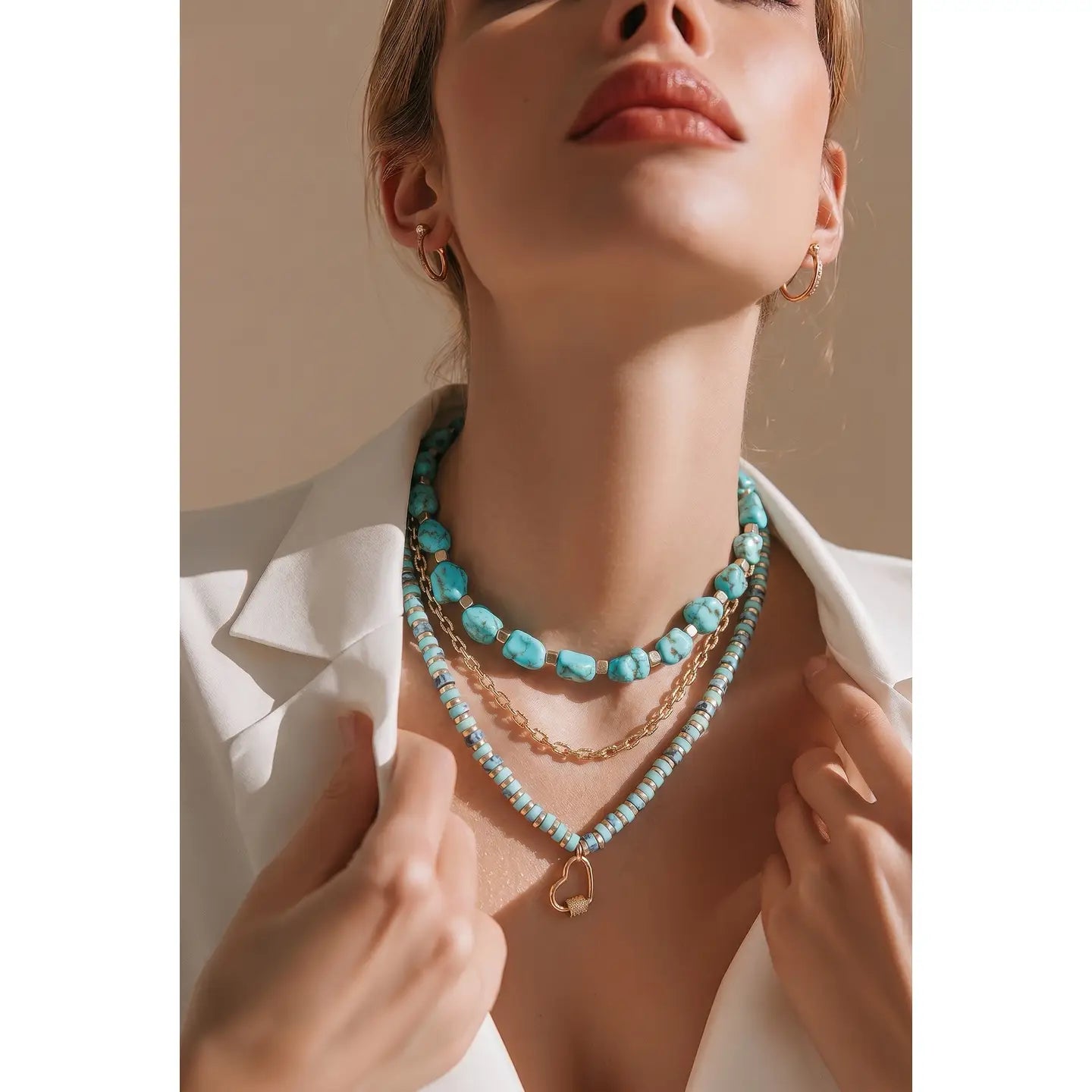 Layered turquoise bead necklace with gold chain and small heart charm on white background.