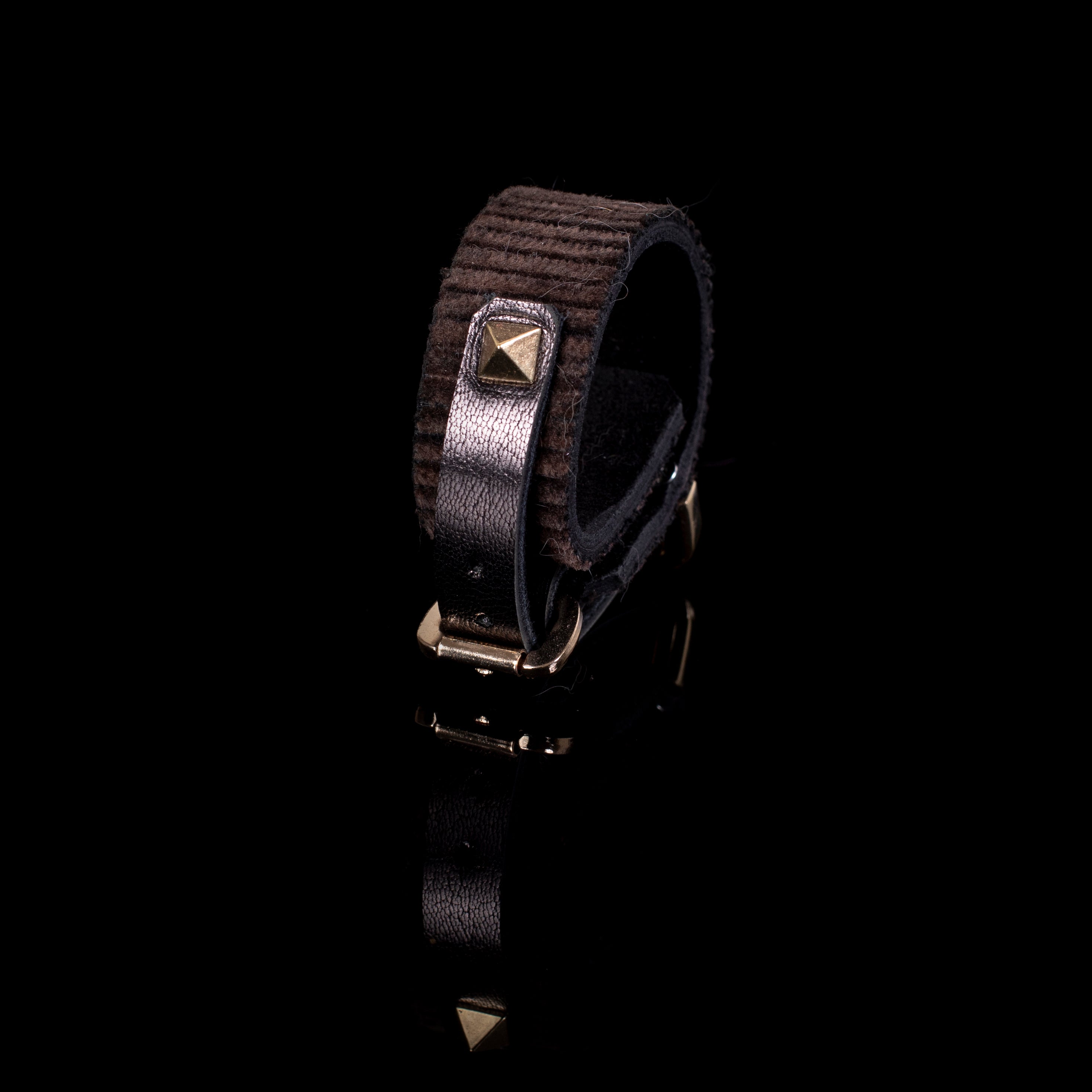 Brown textured leather cuff bracelet with ribbed surface, central strap detail, and gold pyramid stud, minimalist statement piece
