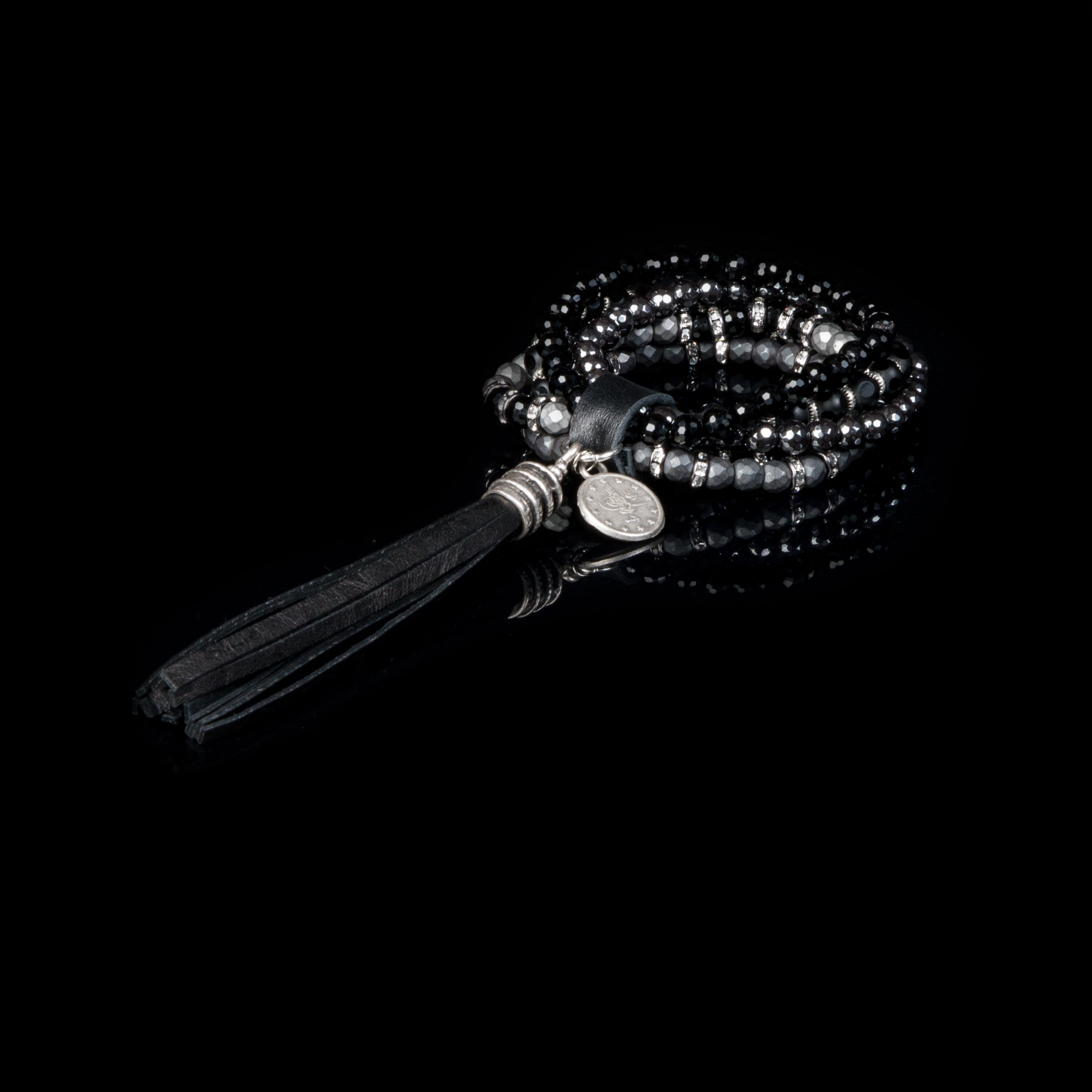 Women’s black layered crystal wrap bracelet with smoky gray bead accents, silver details, and oversized black leather tassel on white background