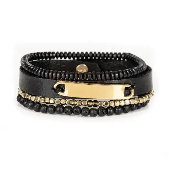 Men’s layered bracelet set featuring a black leather cuff with a polished gold-tone ID plate, matte black lava stone beads, gold-tone hematite spacer beads, and black heishi beads, stacked in a sophisticated black and gold luxury design on a white background.