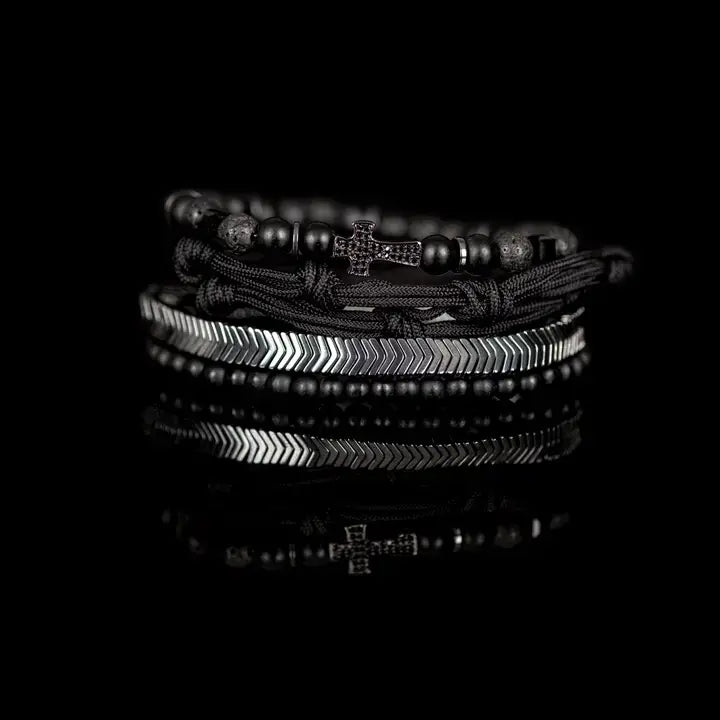 Black layered men’s bracelet set with pavé cross detail, silver chevron metal strand, lava stone beads, matte black beads, and braided rope wraps on white background.