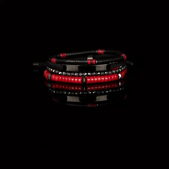 Men’s layered bracelet set featuring black and red heishi beads, faceted hematite crystal beads, black braided cord, a gunmetal ID bar centerpiece, and black accent beads, stacked in a bold contemporary luxury design on a white background.