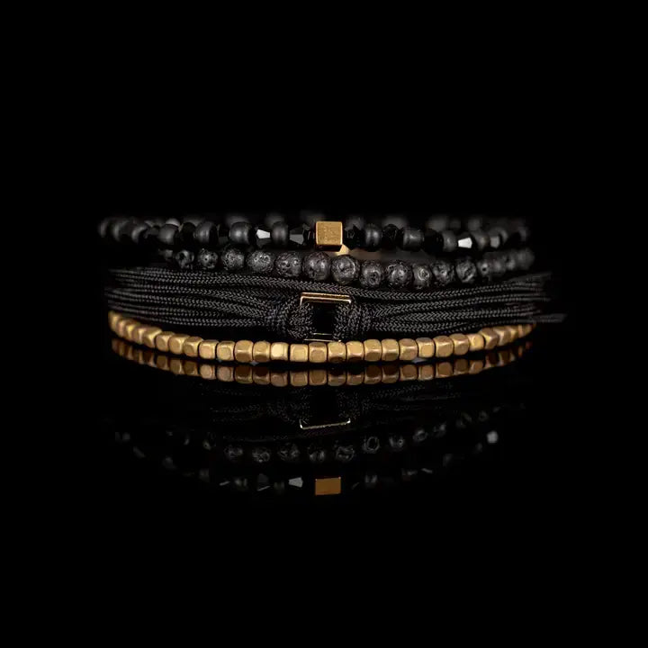 Black and gold layered men’s bracelet set with lava stone beads, gold cube accents, faceted black beads, braided rope wraps, and metallic centerpiece on white background.