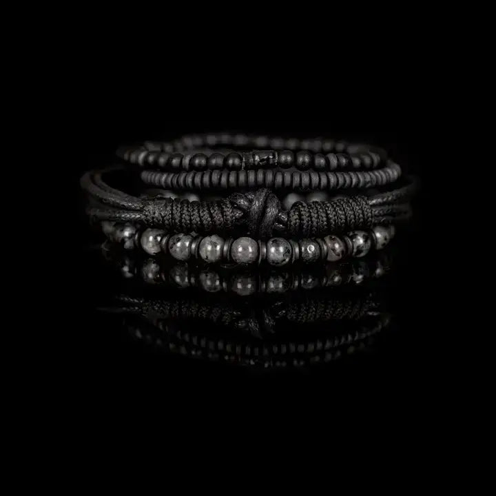 Black layered men’s bracelet set with matte black beads, braided rope wraps, and gray marbled stone accents on white background.
