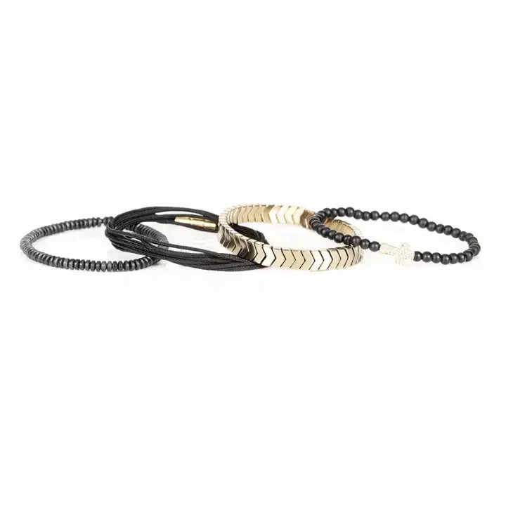 Black multi-layer men’s bracelet set with matte black beads, gold chevron metal bar, black cords, and cross accent detail on white background.