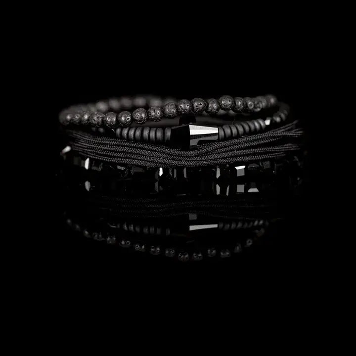Black layered men’s bracelet set with lava stone beads, geometric crystal cube accents, matte black beads, polished centerpiece, and braided rope wraps on white background.