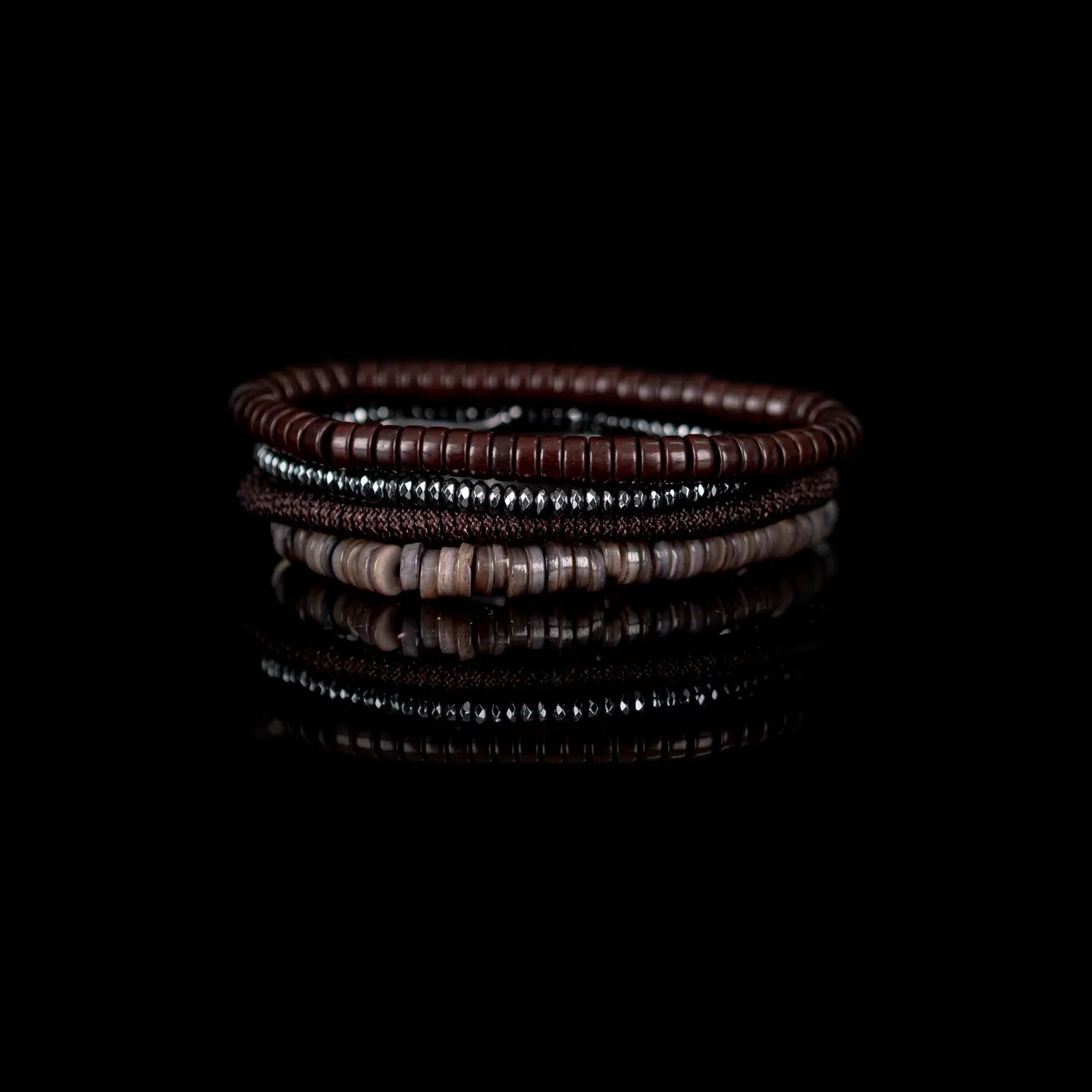 Men's layered bracelet set featuring dark brown heishi beads, faceted hematite spacer beads, brown woven cord detailing, and taupe natural stone disc beads arranged in a minimalist stacked design on a white background.