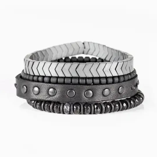 Men’s layered bracelet set featuring a silver-tone chevron stretch bracelet, black leather cuff with gunmetal stud details, matte black bead strand, and faceted black stone beads, stacked in a rugged contemporary luxury design on a white background.