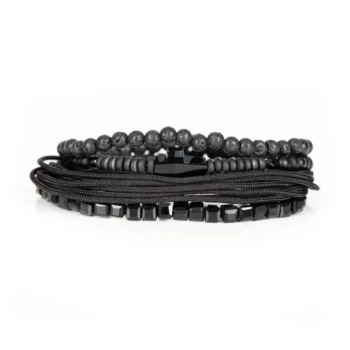 Black layered men’s bracelet set with lava stone beads, geometric crystal cube accents, matte black beads, polished centerpiece, and braided rope wraps on white background.